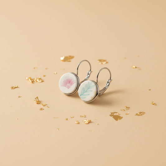 Schrägansicht der handgeschliffenen "Amicitia" Porzellanohrringe von EDELATELIER. im individuellen Duo-Design auf beigem Untergrund mit Blattgold-Partikeln.
