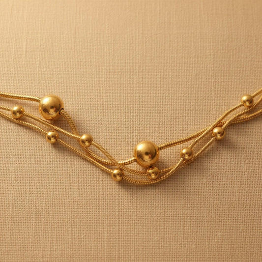 Detailaufnahme der Piccola Perla Halskette mit feinen Strängen und goldfarbenen Kugeln.