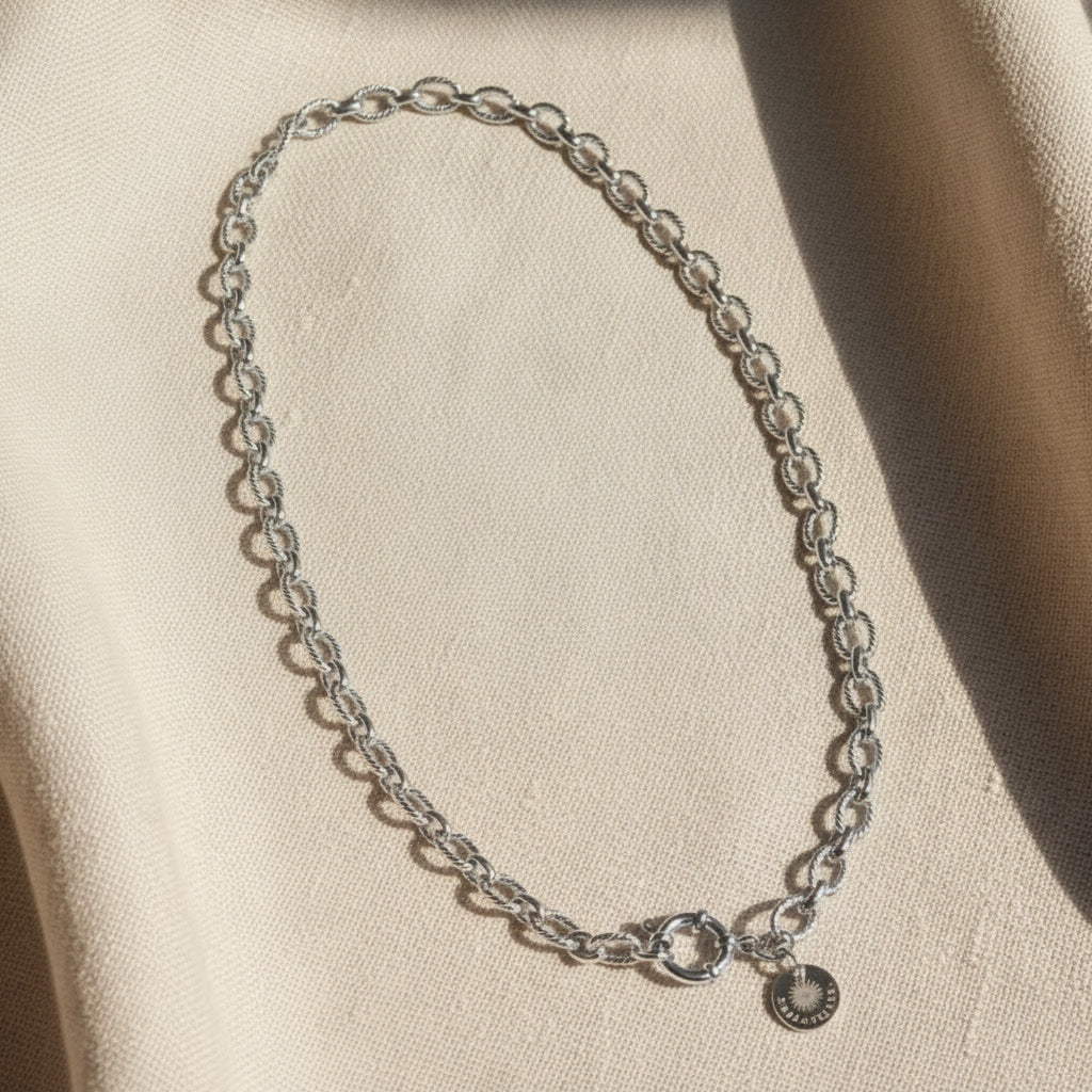 Maglia Gliederkette silberfarben auf hellem Leinen, mit rundem Verschluss und EDELATELIER-Plättchen.
