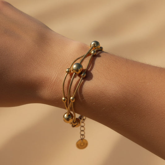 Goldfarbenes Piccola Perla Armband mit feinen Kugeldetails als Tragefoto am Handgelenk im warmen Sonnenlicht.