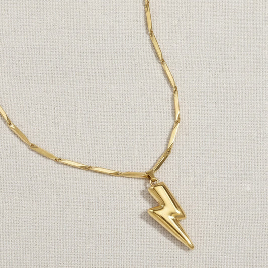 Nahaufnahme der goldfarbenen Saetta Halskette mit Blitzanhänger und strukturierter Gliederkette auf hellem Leinen.