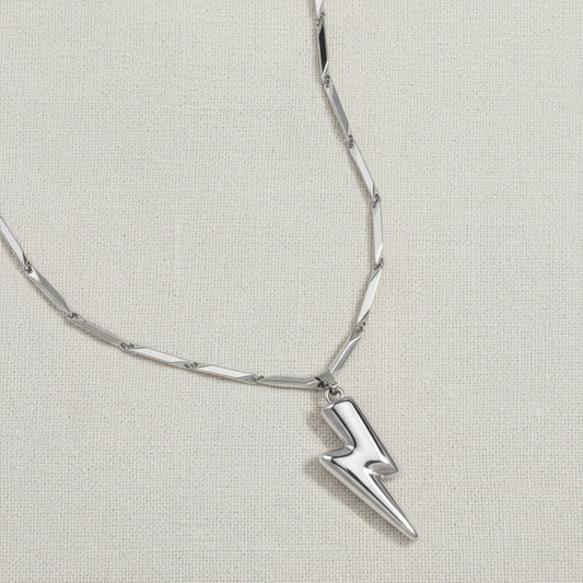 Detailaufnahme der silberfarbenen Saetta Halskette mit Blitzanhänger auf hellem Leinenstoff.