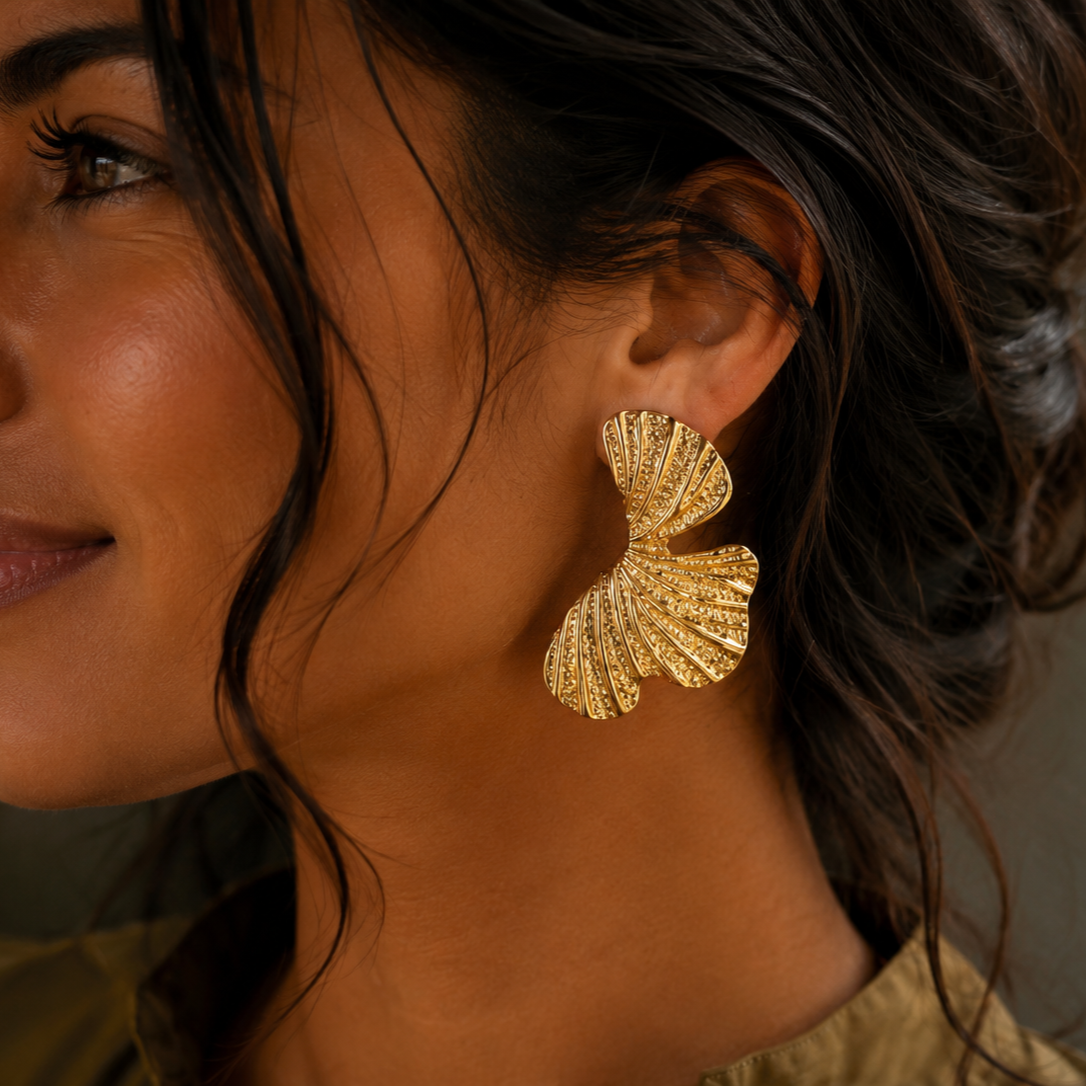 Model trägt goldfarbene Foglia Ohrringe aus Edelstahl in Blattform.