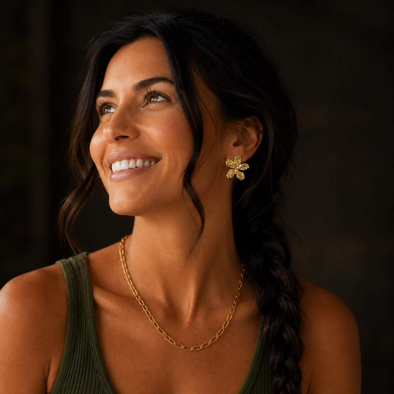 Lächelndes Model trägt goldene Blütenohrringe und eine goldene Kette.