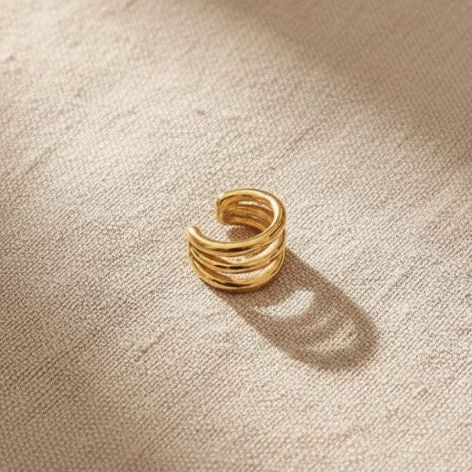Goldener Intreccio Ear Cuff auf beigem Leinenstoff.