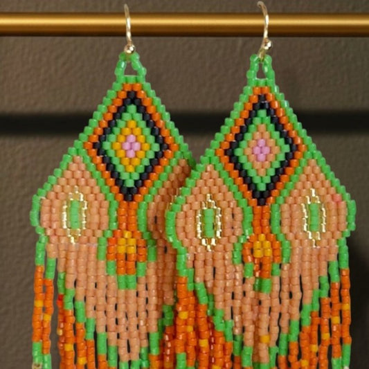 Handgewebte Miyuki Perlenohrringe Modell Tramonto Etrusco von EDELATELIER. in Nahaufnahme, mit geometrischem Muster in Terrakotta, Blattgrün und Gold, ca. 8,5 cm lang, vor einem dunklen Hintergrund, hängend an einer goldenen Stange.