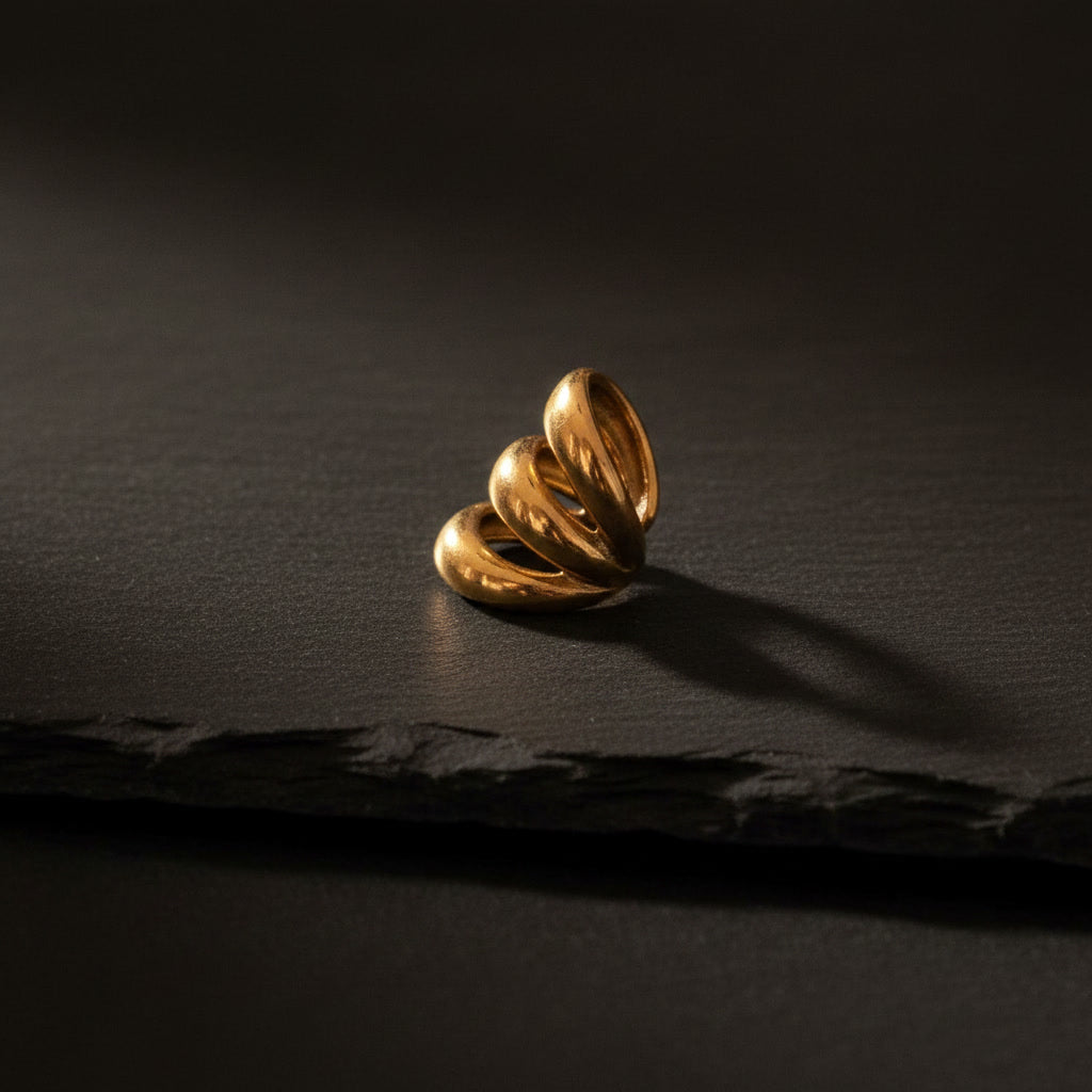 Goldener Ear Cuff ohne Ohrloch mit geschwungener dreifacher Form auf schwarzem Hintergrund.