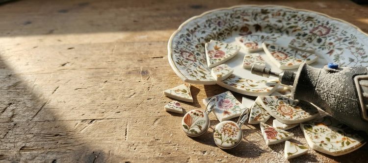 Porzellanohrringe aus handgeschliffenem Vintage-Porzellan auf rustikalem Holztisch mit Porzellanscherben und Werkzeug im warmen Licht.