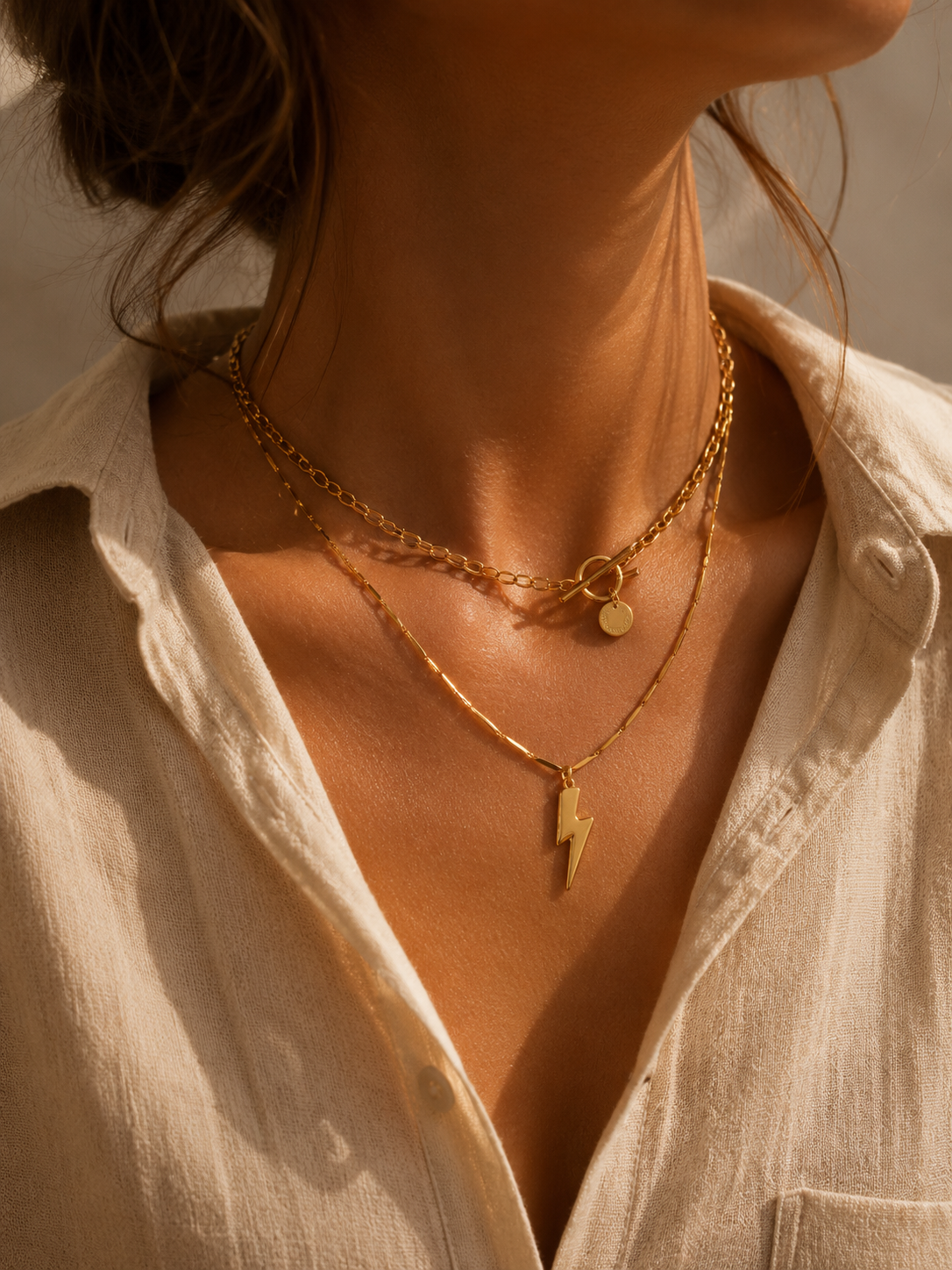 Goldfarbene Edelstahl-Halsketten im Layering-Look auf warmer Haut mit heller Bluse.