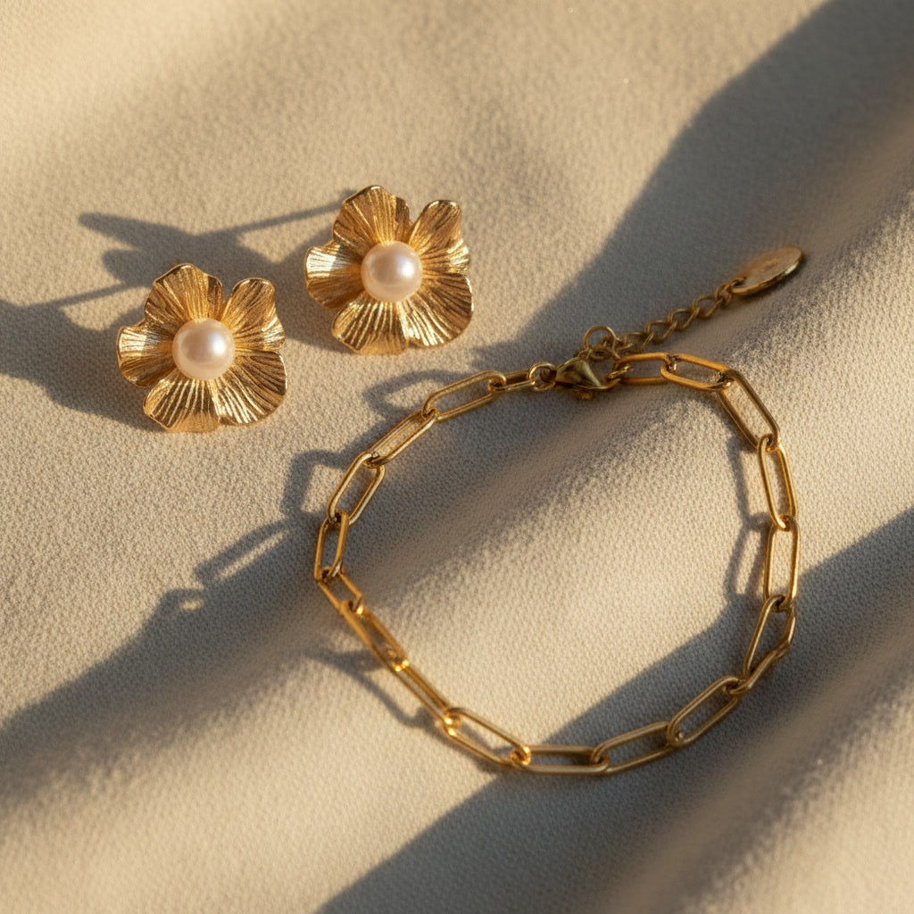 Fiore Blütenohrringe mit Perle kombiniert mit goldenem Armband auf hellem Stoff.