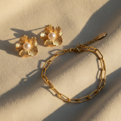 Fiore Blütenohrringe mit Perle kombiniert mit goldenem Armband auf hellem Stoff.