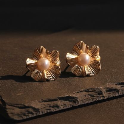 Fiore Blütenohrringe in Goldfarben mit Perle auf schwarzem Hintergrund.