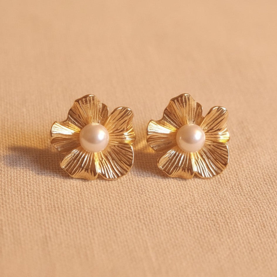 Fiore Blütenohrringe mit Perle kombiniert mit goldenem Armband auf hellem Stoff.