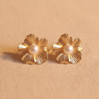 Fiore Blütenohrringe mit Perle kombiniert mit goldenem Armband auf hellem Stoff.