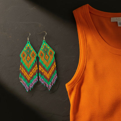 Gemini hat gesagt
Handgemachte Perlenohrringe Sogno d’Oriente von EDELATELIER.: Handgewebte Statement-Ohrringe mit geometrischem Muster in Grün, Ocker und Braun, präsentiert in einem stimmungsvollen Flatlay auf dunklem Untergrund neben einem orangefarbenen Oberteil.