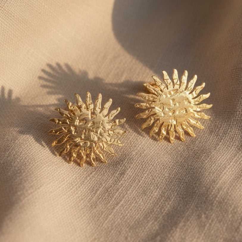 Goldene Sonnenohrringe auf beigem Untergrund in Nahaufnahme.