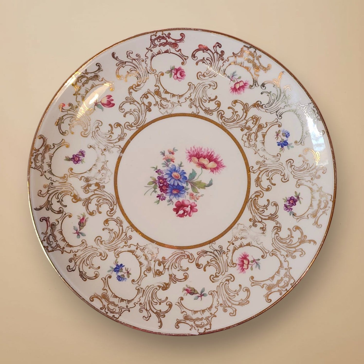 Ein antiker Porzellanteller mit filigranem Blumendekor und Goldrand, der als Ausgangsmaterial für die Ohrringe dient. Das Motiv der pinkfarbenen Pfingstrose in der Mitte zeigt den Ursprung und die Geschichte des Unikats von EDELATELIER.