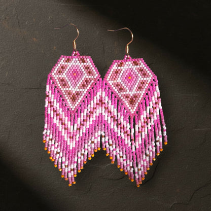 Detailansicht der handgefertigten Ohrringe Alba Dorata. Die fokussierte Beleuchtung betont die luxuriöse Webkunst der japanischen Miyuki Delica Perlen in Gold und Pink sowie die geometrische Präzision des Designs.