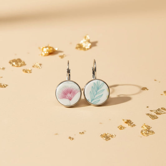 Frontalaufnahme der EDELATELIER. Porzellanohrringe "Amicitia" im harmonischen Duo-Design mit rosa Blüte und grünem Blatt-Motiv auf hellem Untergrund mit Blattgold-Dekoration.