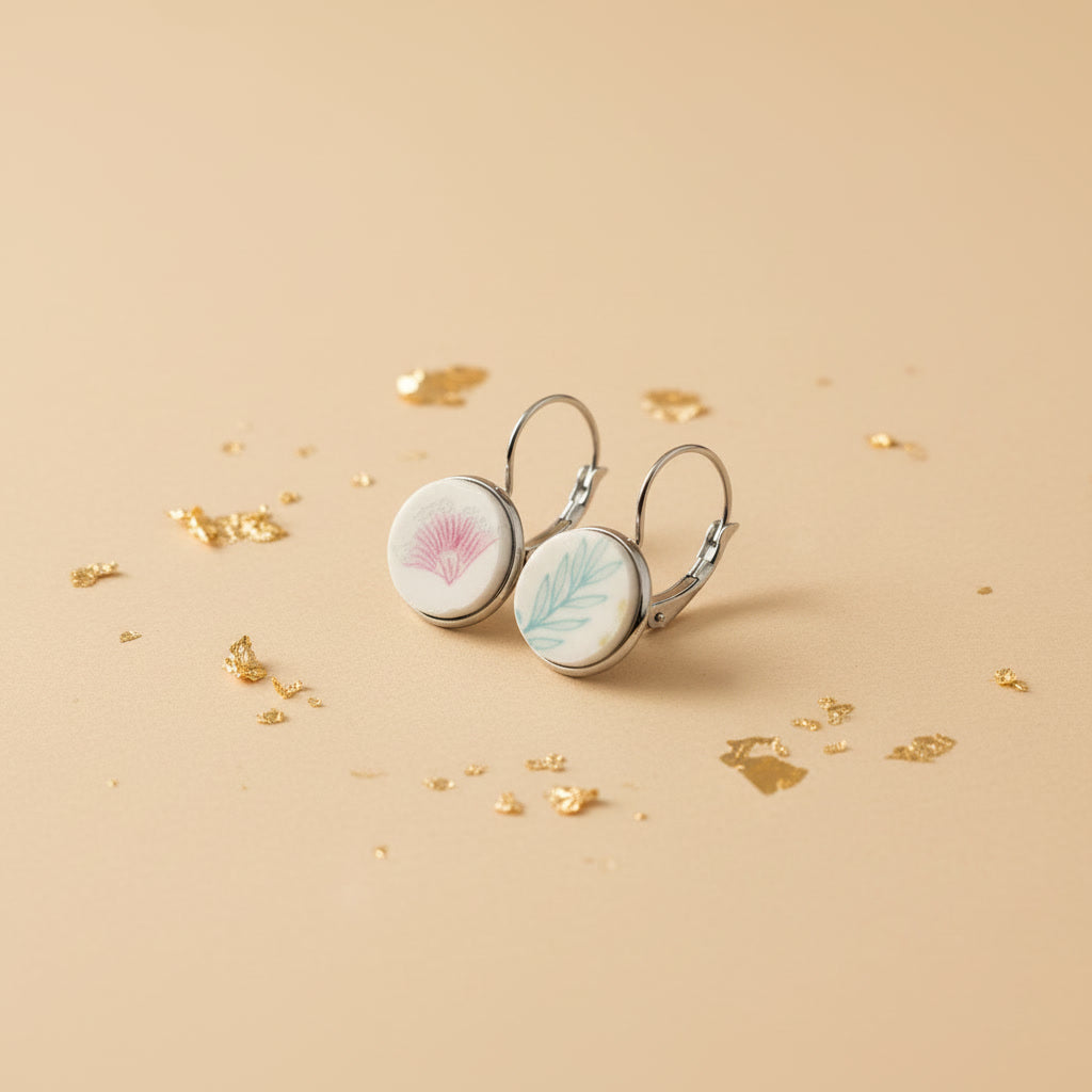Schrägansicht der handgeschliffenen "Amicitia" Porzellanohrringe von EDELATELIER. im individuellen Duo-Design auf beigem Untergrund mit Blattgold-Partikeln.