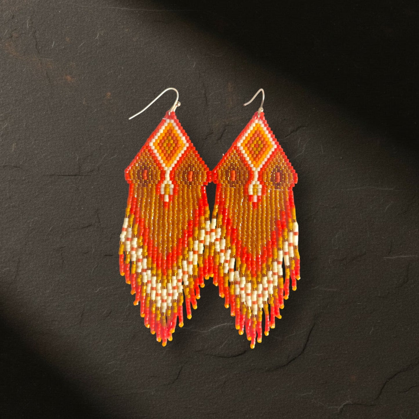 Ein Paar handgewebte Boho-Ohrringe Arancia d'Oro von EDELATELIER. aus Miyuki-Perlen in Orange und Gold, frontal fotografiert auf einer dunklen Schieferplatte.