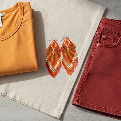 Ein modisches Arrangement auf einem beigen Leinentuch. Im Zentrum liegen die beiden Perlenohrringe aus den vorherigen Bildern. Links ist ein gefaltetes, senfgelbes T-Shirt zu sehen, rechts ein roter Jeansrock Die Komposition ist harmonisch und zeigt, wie die Ohrringe mit verschiedenen Outfits kombiniert werden können.
