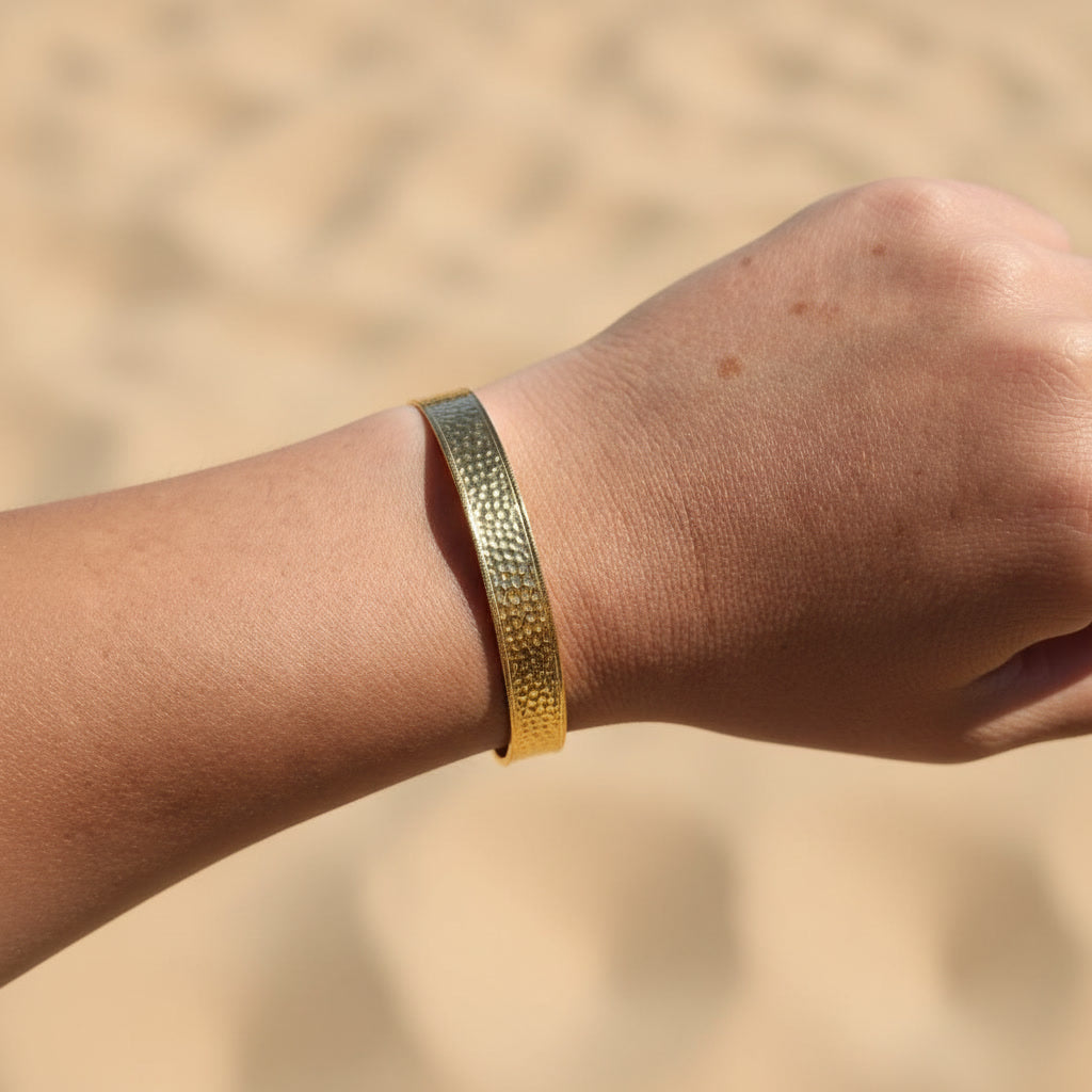 Aurelia Armreif Gold am Handgelenk getragen, breiter gehämmerter Edelstahl-Armreif in 18 Karat PVD Gold.