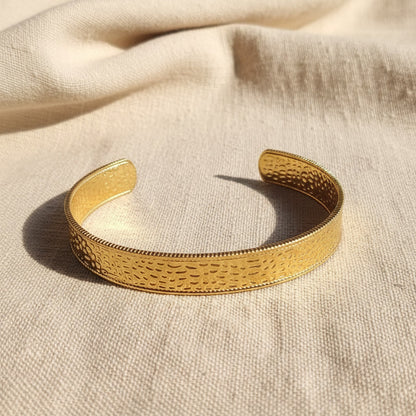 Aurelia breiter gehämmerter Armreif Gold aus 18 Karat PVD-vergoldetem 316L Edelstahl auf beigem Leinen.