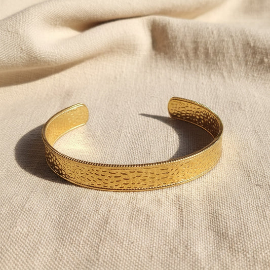 Aurelia breiter gehämmerter Armreif Gold aus 18 Karat PVD-vergoldetem 316L Edelstahl auf beigem Leinen.