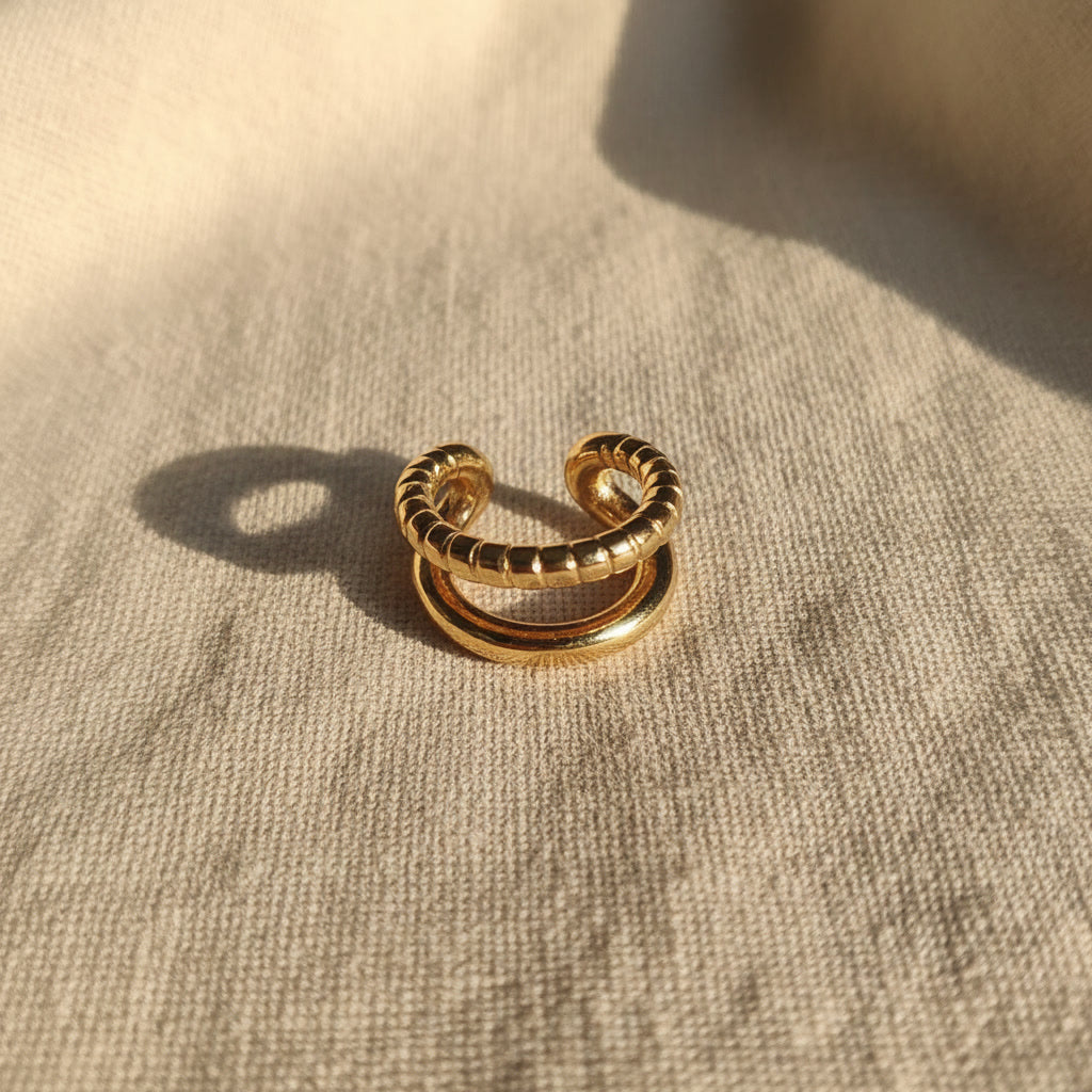 Goldfarbener Ear Cuff Aureus aus Edelstahl mit 18K PVD-Vergoldung auf beigem Leinenstoff – zweireihiges Design mit glatter und strukturierter Oberfläche.