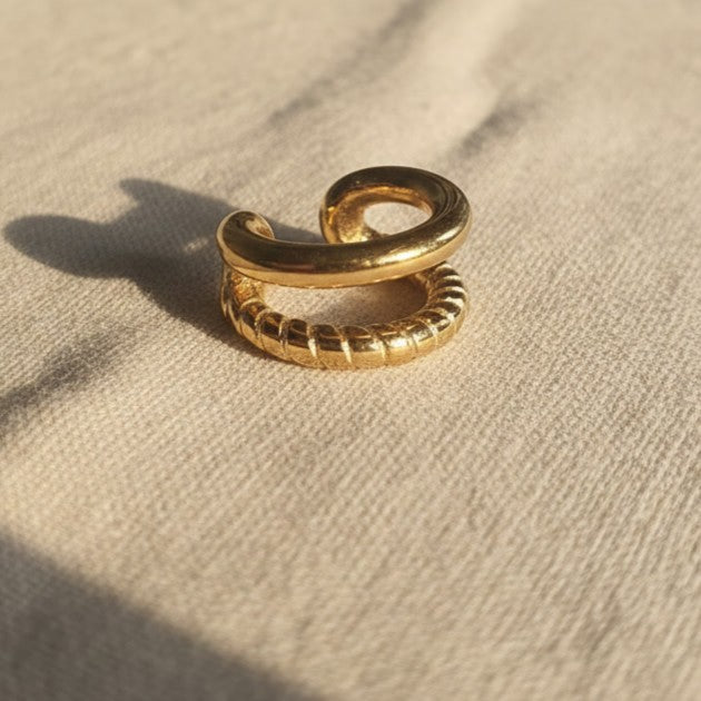 Goldfarbener Ear Cuff Aureus aus Edelstahl mit 18K PVD-Vergoldung auf beigem Leinenstoff – zweireihiges Design mit glatter und strukturierter Oberfläche.