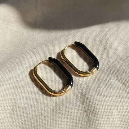 Nera Creolen Gold Schwarz aus 18 Karat PVD-vergoldetem Edelstahl mit schwarzem Resin auf beigem Leinen.