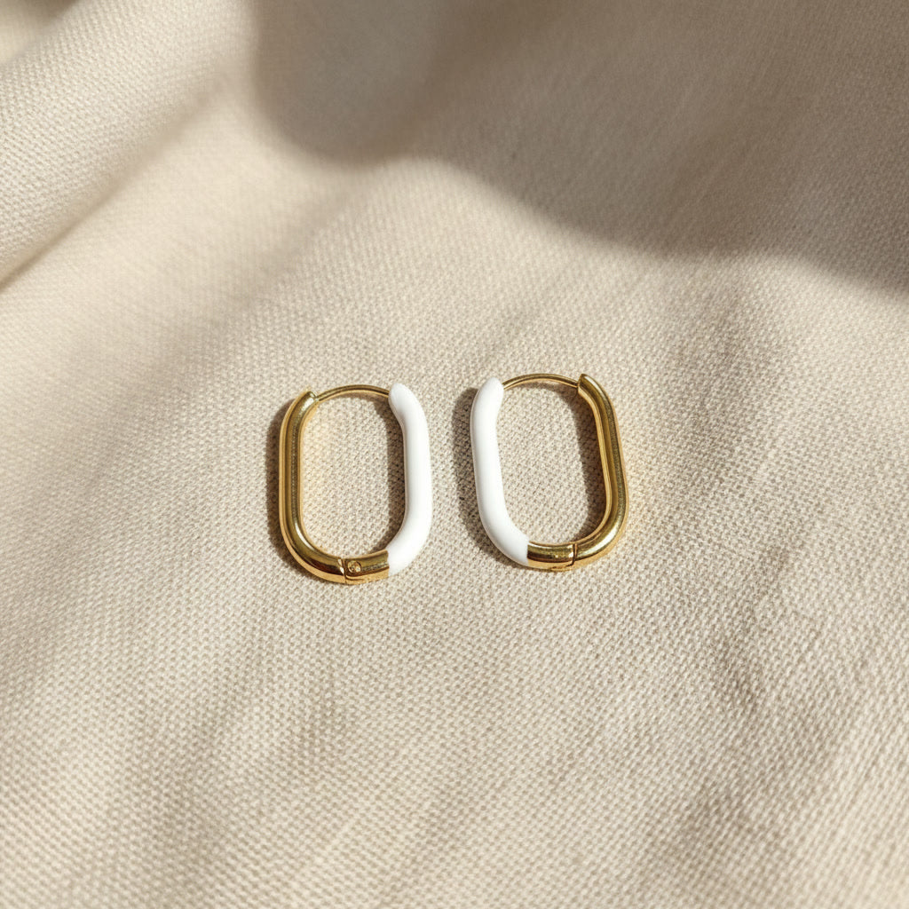 Bianca Creolen Gold Weiß frontal auf beigem Leinen, ovale Form und weißer Epoxidharz-Akzent sichtbar.