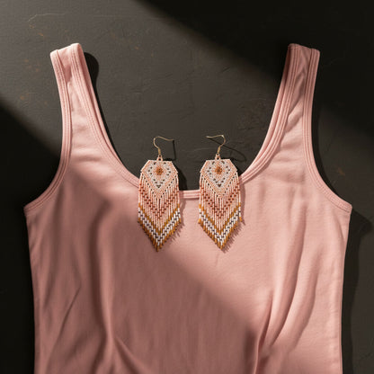 Die handgewebten Statement-Ohrringe Bianco Pesca von EDELATELIER. in zarten Pastellfarben, präsentiert auf einem rosa Top vor dunklem Hintergrund mit stimmungsvollem Lichteinfall.