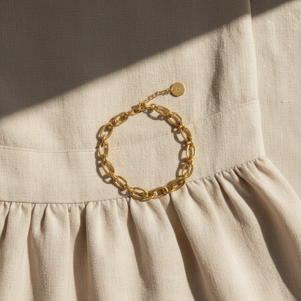 Goldfarbenes Catena Armband auf beigem Leinenkleid im Sonnenlicht.