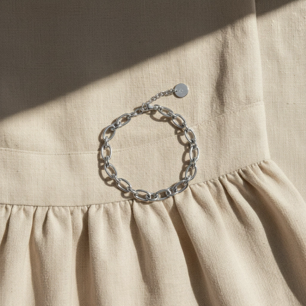 Silberfarbenes Catena Armband auf beigem Leinenkleid im Sonnenlicht.