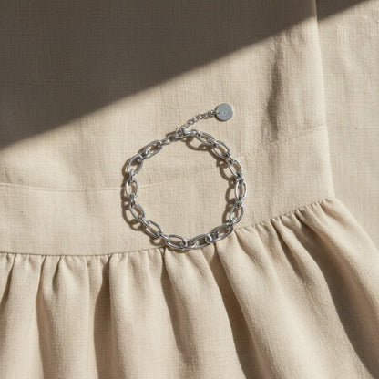 Silberfarbenes Catena Armband auf beigem Leinenkleid im Sonnenlicht.