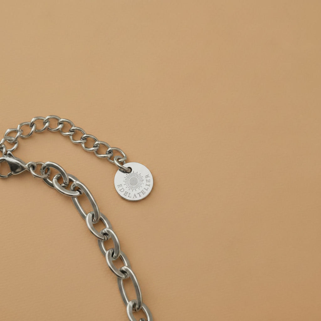 Detailaufnahme der silberfarbenen Edelstahlkette mit Verlängerungskette und EDELATELIER. Logoplättchen.