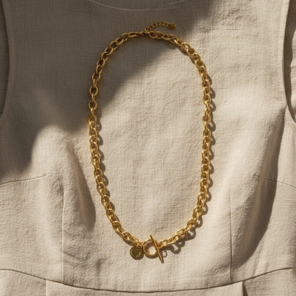 Catena Luce Halskette goldfarben auf beigem Leinenkleid im Sonnenlicht.