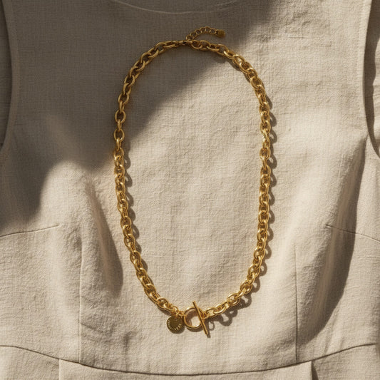 Catena Luce Halskette goldfarben auf beigem Leinenkleid im Sonnenlicht.