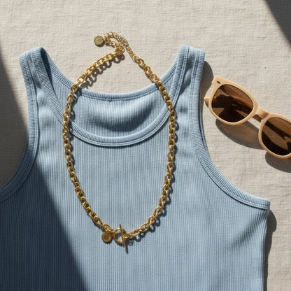 Catena Luce Halskette goldfarben auf blauem Top mit Sonnenbrille im Sommerlook.