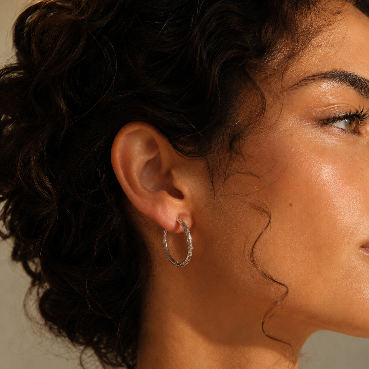 Cerchio Creolen in Silber am Ohr eines Models mit dunklen Locken