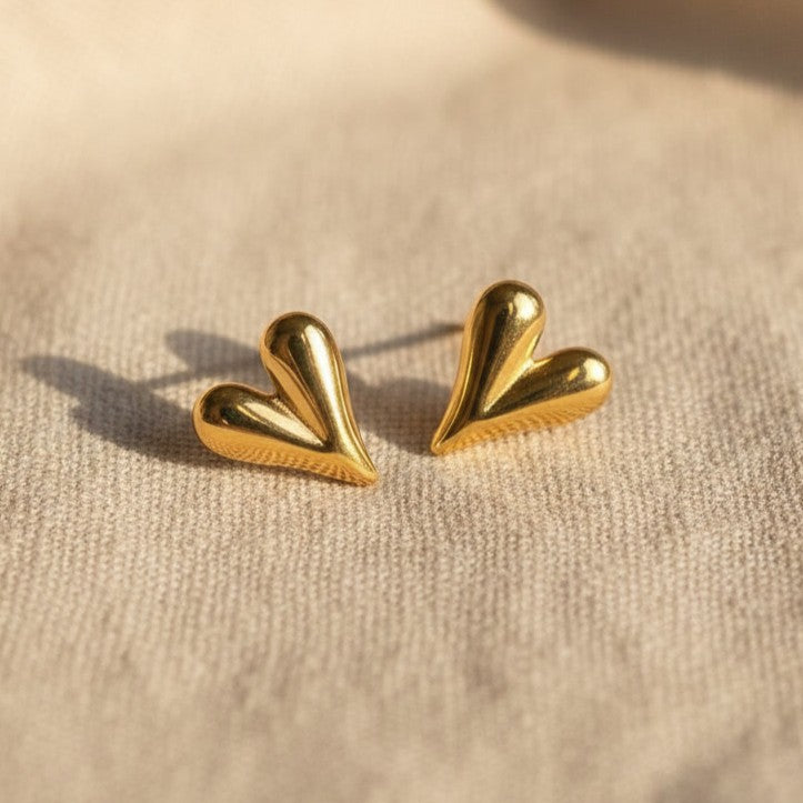 Cuore Piccolo Herzohrringe in Gold auf hellbeigem Leinenuntergrund. Lechte Lichteinstrahlung von der Seite kommend. 