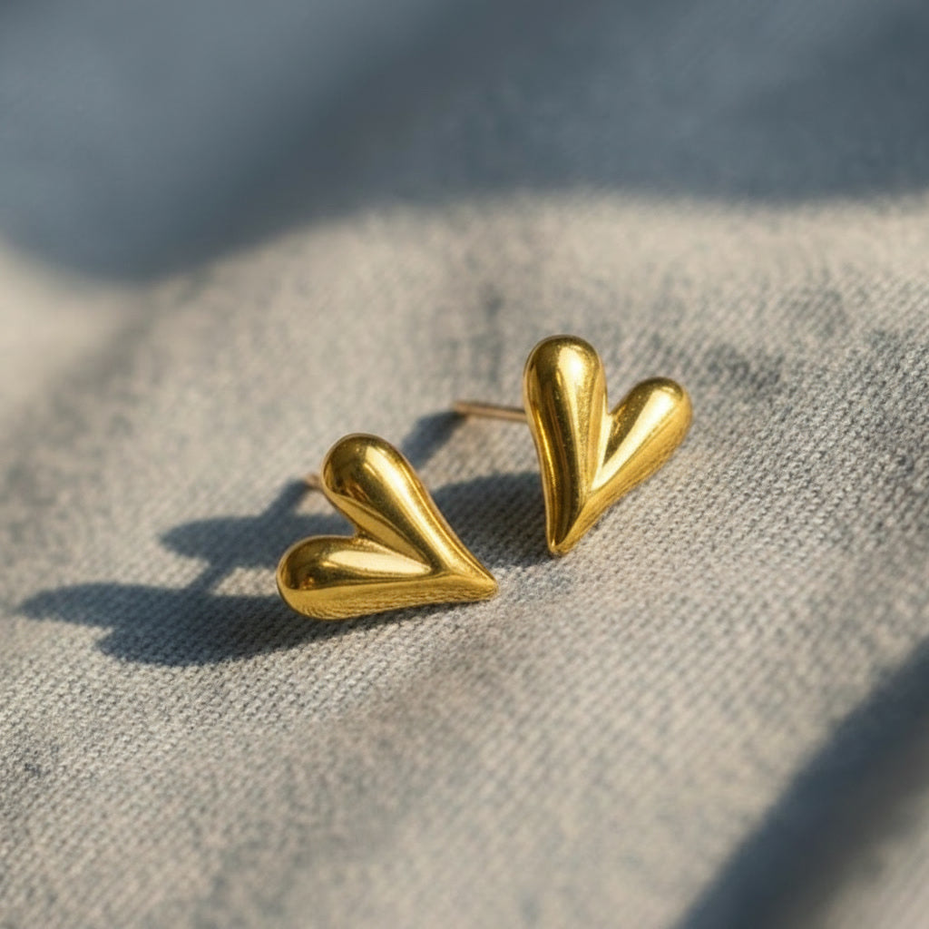 Goldfarbene Cuore Piccolo Herzohrringe auf hellem Stoff.