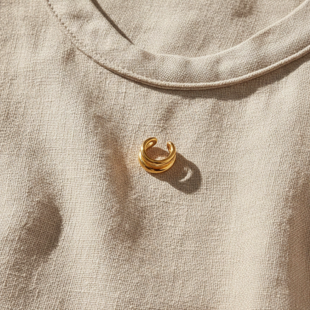 Goldener Doppio Ear Cuff auf hellem Leinenstoff.