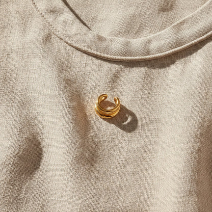 Goldener Doppio Ear Cuff auf hellem Leinenstoff.