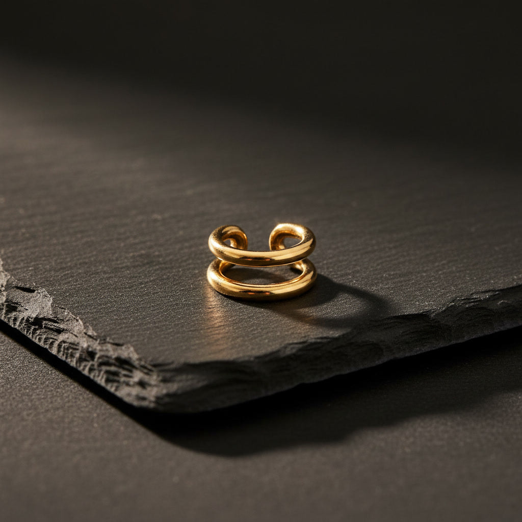 Goldener Doppio Ear Cuff aus Edelstahl auf dunklem Schiefer.
