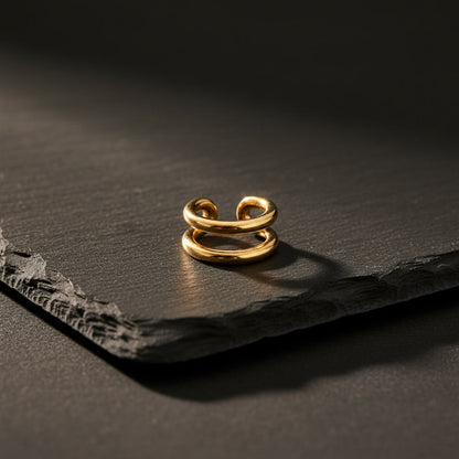 Goldener Doppio Ear Cuff aus Edelstahl auf dunklem Schiefer.