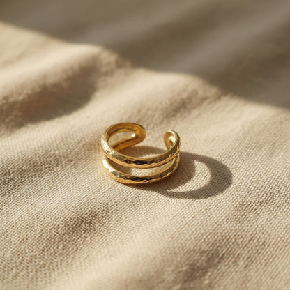 Gehämmerter Ear Cuff Martellato aus 14K vergoldetem Edelstahl auf beigem Leinen.