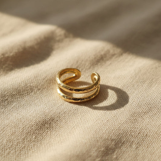 Gehämmerter Ear Cuff Martellato aus 14K vergoldetem Edelstahl auf beigem Leinen.